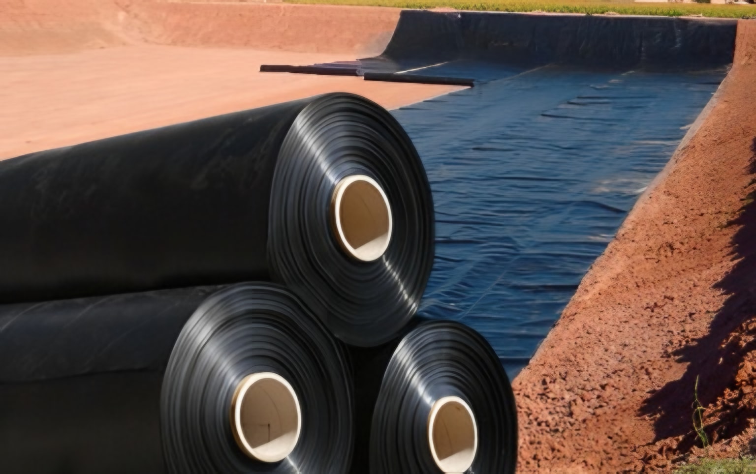 Rollos de geomembrana HDPE junto a una cubeta en instalación